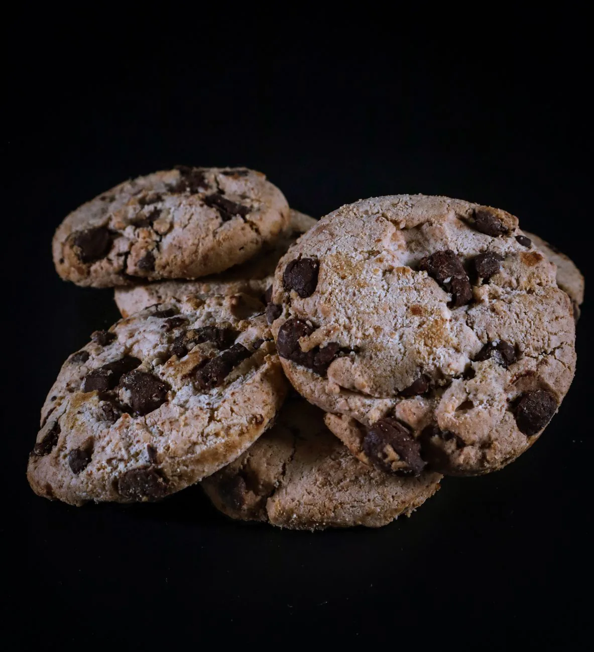 Stacked chocolate chip cookies on a dark surface